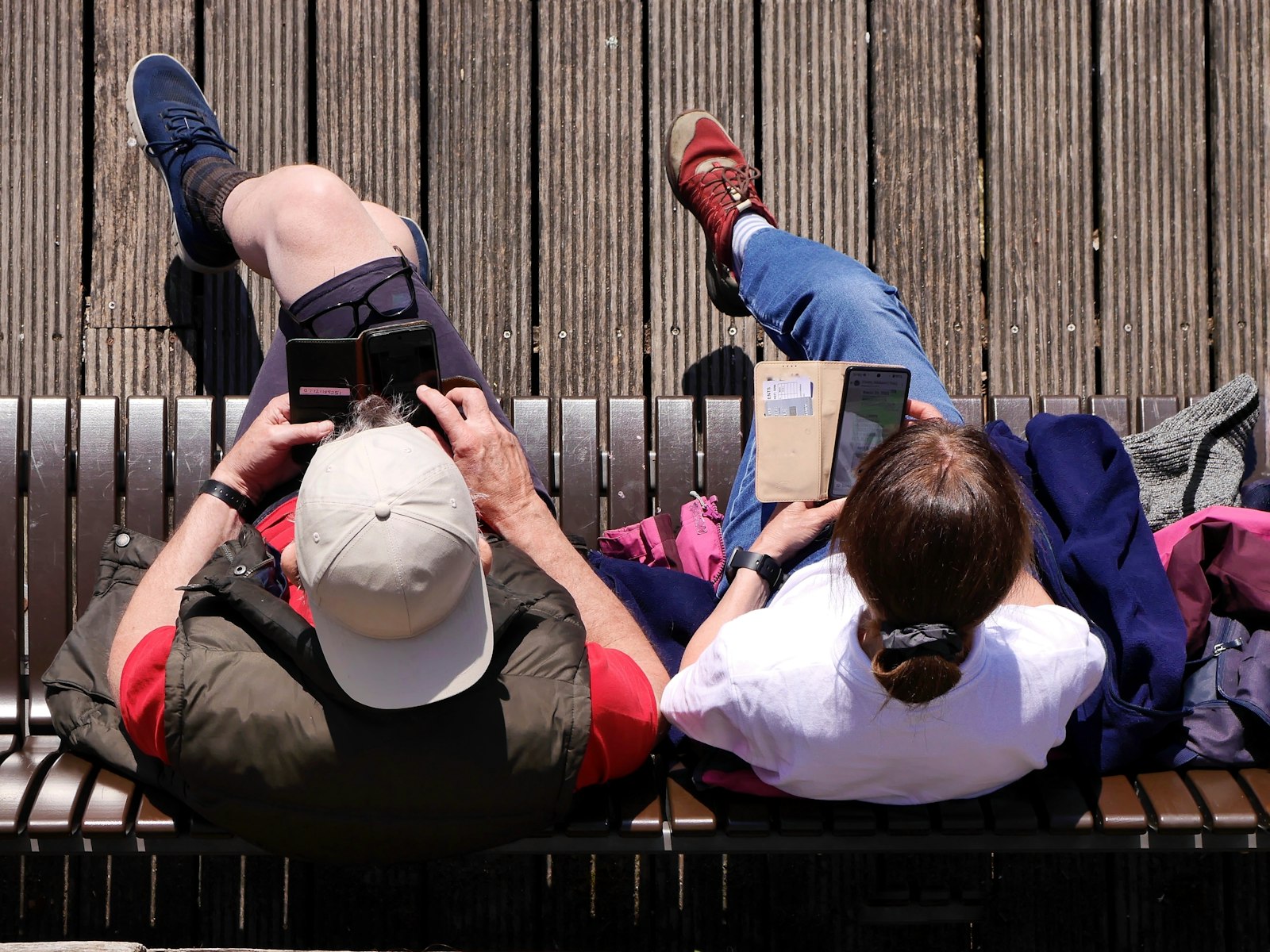 Twee mensen op een bankje, van bovenaf gezien, elk bezig op hun telefoon
